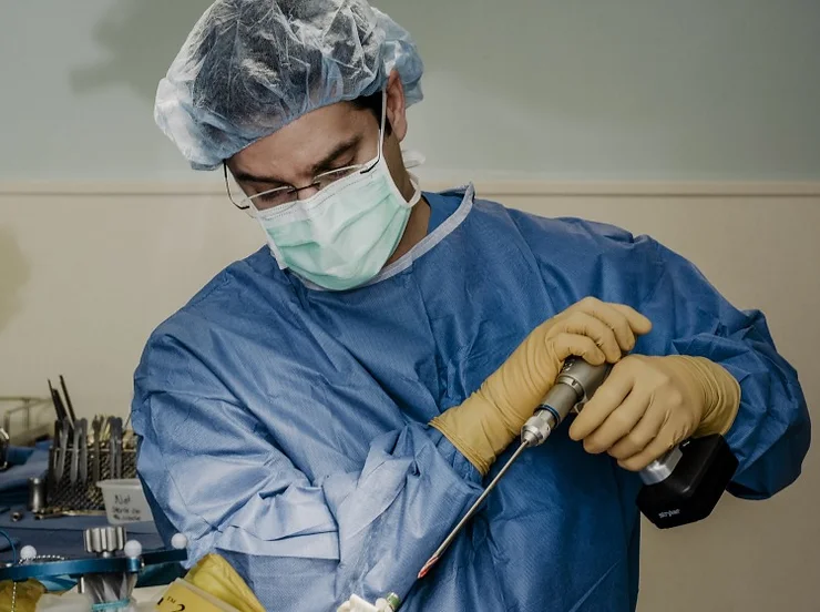 Male surgeon in blue scrubs wearing a mask using a drill