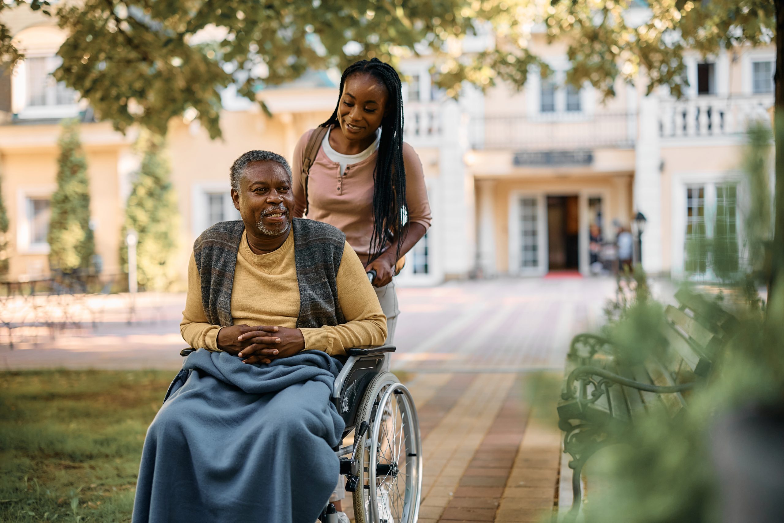 Home caregiver and senior man on a wheelchair, walking outdoors